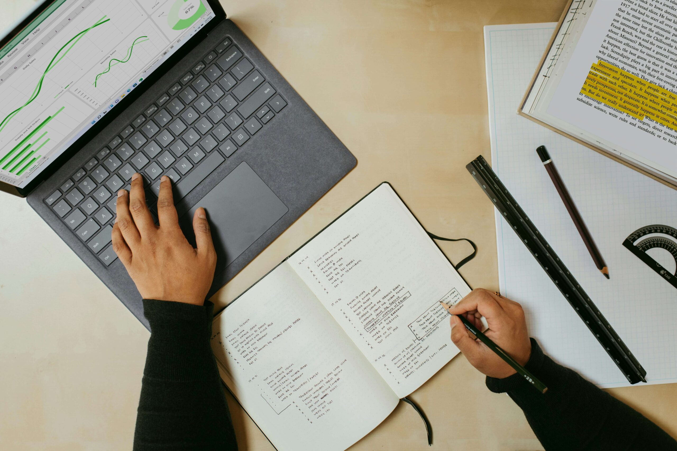 Small business owner planning operations strategy in a notebook alongside a laptop displaying business performance charts.